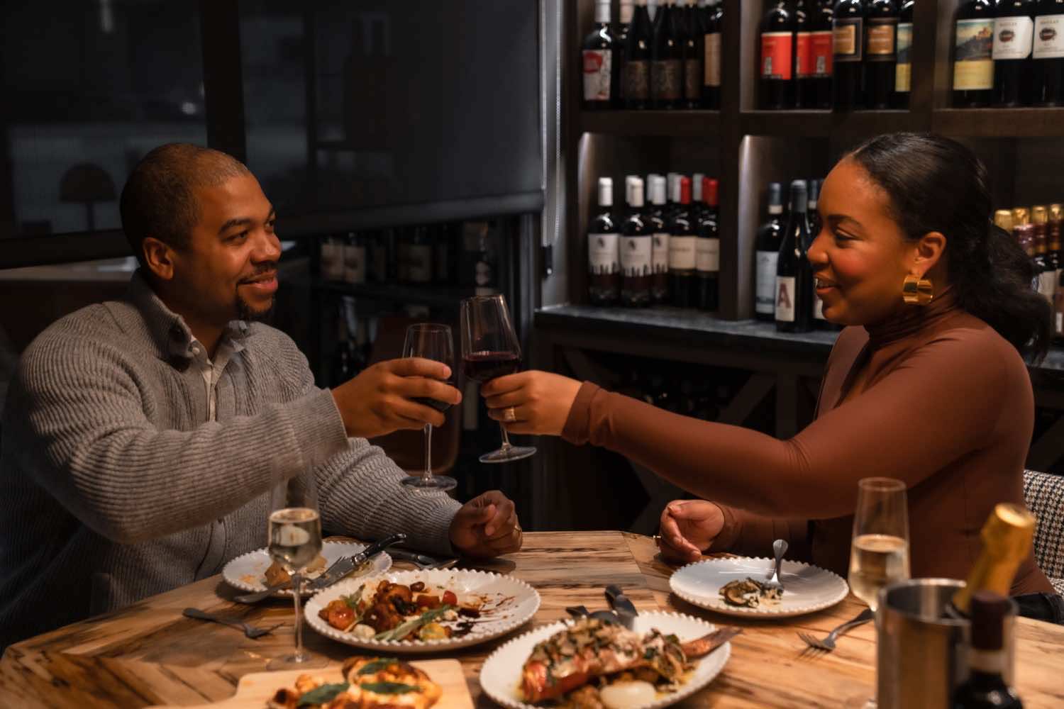 couple touching wine glasses together at a table in a wine bar
